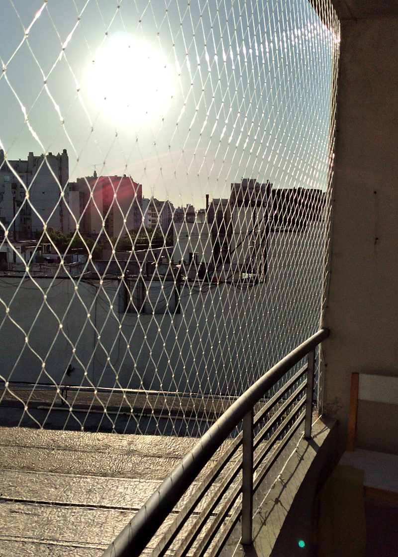 Red de seguridad en balcón de edificio, vista a la ciudad a contraluz